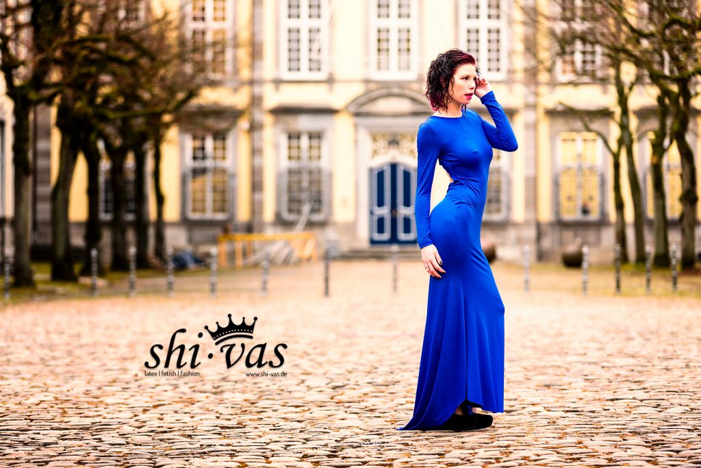 Seitliche Aufnahme von Coco auf Kopfsteinpflaster vor dem Schloss; die Nippelpiercings zeichnen sich deutlich unter dem Stoff ab.