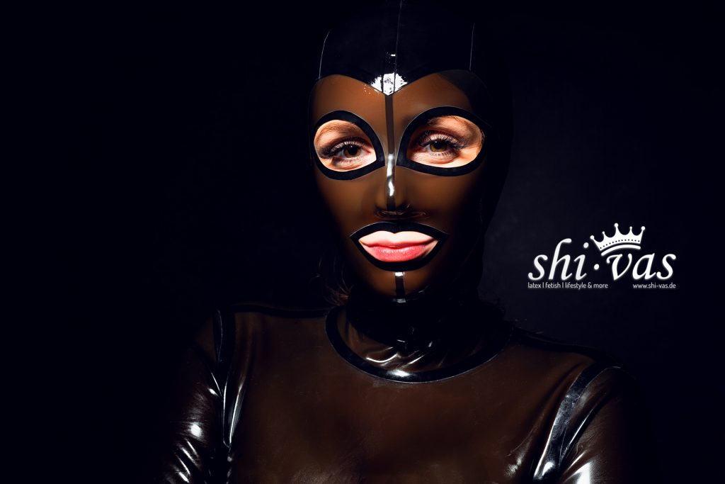 Finnja blickt direkt und herausfordernd in die Kamera, das Schwarz der Maske bildet einen harten Kontrast zum Braun des Kleides.