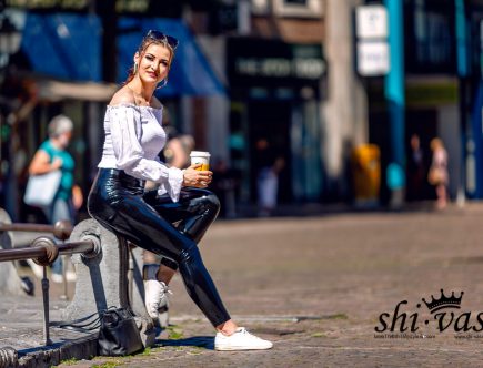 Lina sitzt auf der Steinmauer, hält den Kaffeebecher fest und lächelt freundlich