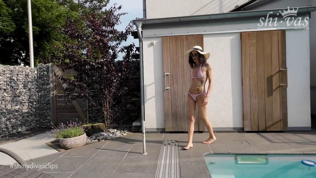 Coco läuft selbstbewusst im rosa Microbikini am Pool entlang, trägt einen Sonnenhut und Sonnenbrille.