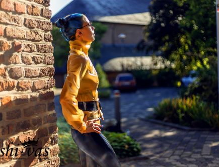 Coco im Profil, sie blickt sehnsüchtig in die Ferne. Man sieht das Tattoo in ihrem Nacken und den hohen Kragen der Bluse.