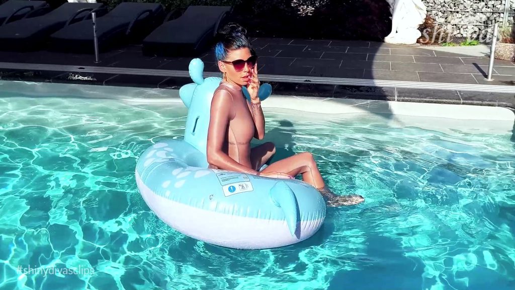 Coco sitzt seitlich auf dem Hippo, Finger am Mund, nachdenklich-erotischer Blick, der nasse Anzug spannt über die Schenkel.