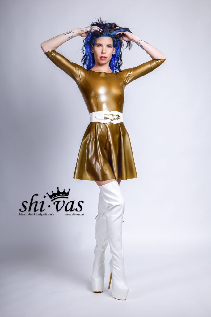 Coco steht frontal, beide Hände sind in ihre blau-schwarzen Haare gegriffen. Sie blickt direkt und herausfordernd in die Kamera.