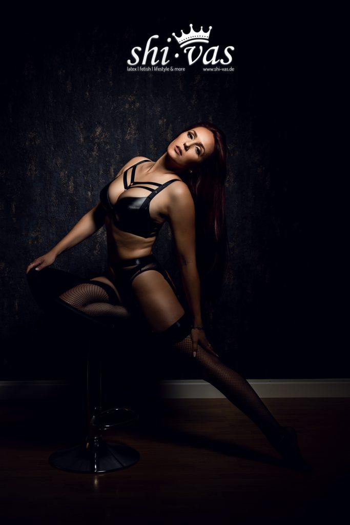 Finnja sitzt auf einem Barhocker, den Oberkörper weit nach hinten gebeugt, den Kopf im Nacken und die Augen geschlossen. Das Licht betont ihre Halspartie und das Dekolleté.