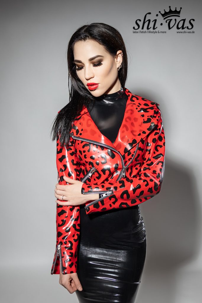 Amy Grey blickt mit geschlossenen Augen nach unten. Die Jacke glänzt im Studiolicht, während sie sanft einen Arm umfasst.