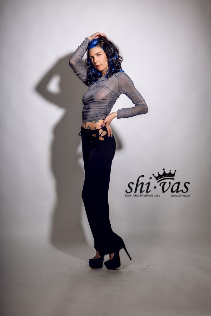 Totale, seitliches Profil, Hüfte nach hinten, rechte Hand auf dem Kopf, linke Hand in die Hüfte gestützt.