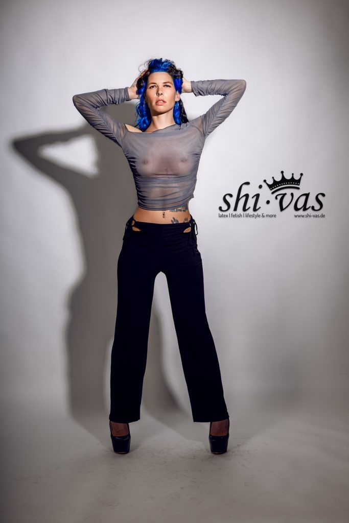 Totale, frontal, breiter Stand, beide Hände hinter dem Kopf verschränkt, Ellbogen weit außen, graues Mesh-Top.