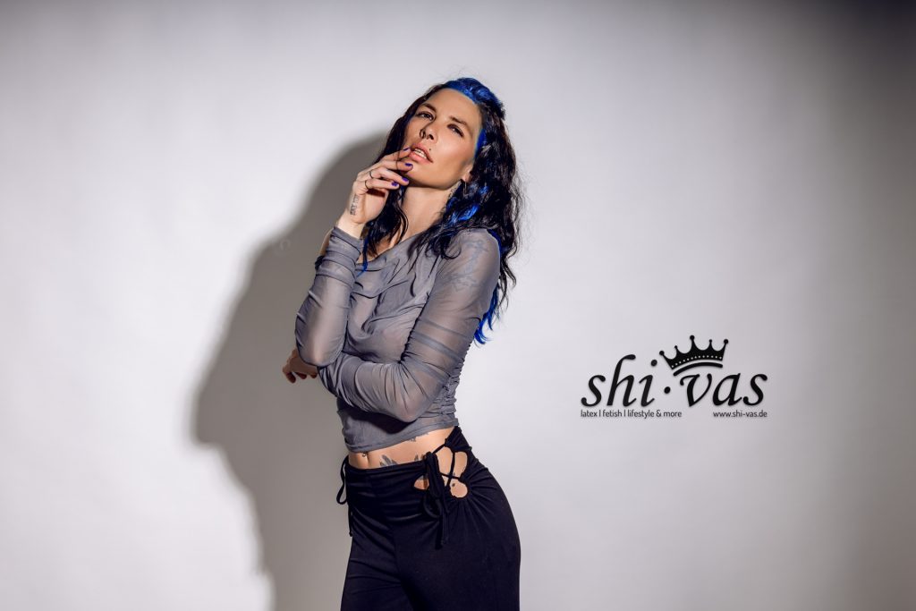 Halbtotal, 3/4 Ansicht schräg, linker Arm quer vor dem Bauch unter der Brust, rechte Hand am Kinn/Lippen mit gespreizten Fingern.