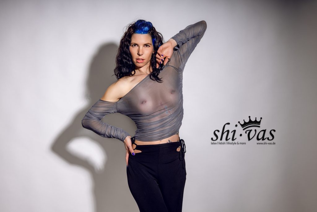 Halbtotal, frontal, Hüfte stark raus, linke Hand fest an der Hüfte, rechte Hand seitlich am Kopf/Ohr angewinkelt.