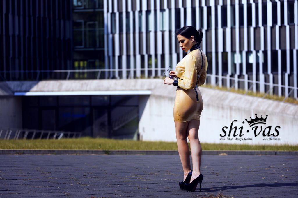 Amy Grey steht mit dem Rücken zur Kamera, blickt leicht über die Schulter. Sie hält ihre Sonnenbrille in den Händen.