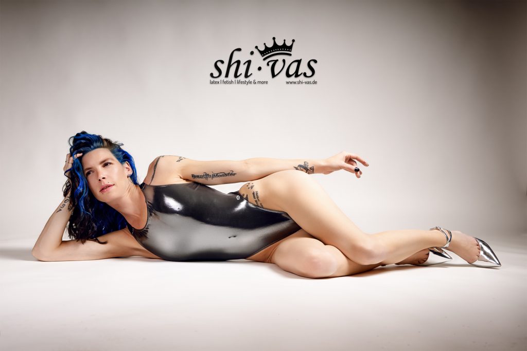 Coco liegt seitlich im silbernen, stark reflektierenden LEOHEX-Swimsuit mit angewinkelten Beinen und silbernen High Heels, Blick zur Seite