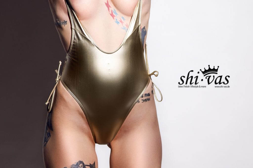 Detailaufnahme des Torsos von Coco im goldenen Realise Poolslider. Der Fokus liegt auf der engen Passform des glänzenden Materials im Schritt und an den Hüften sowie auf den seitlichen Schnürungen.