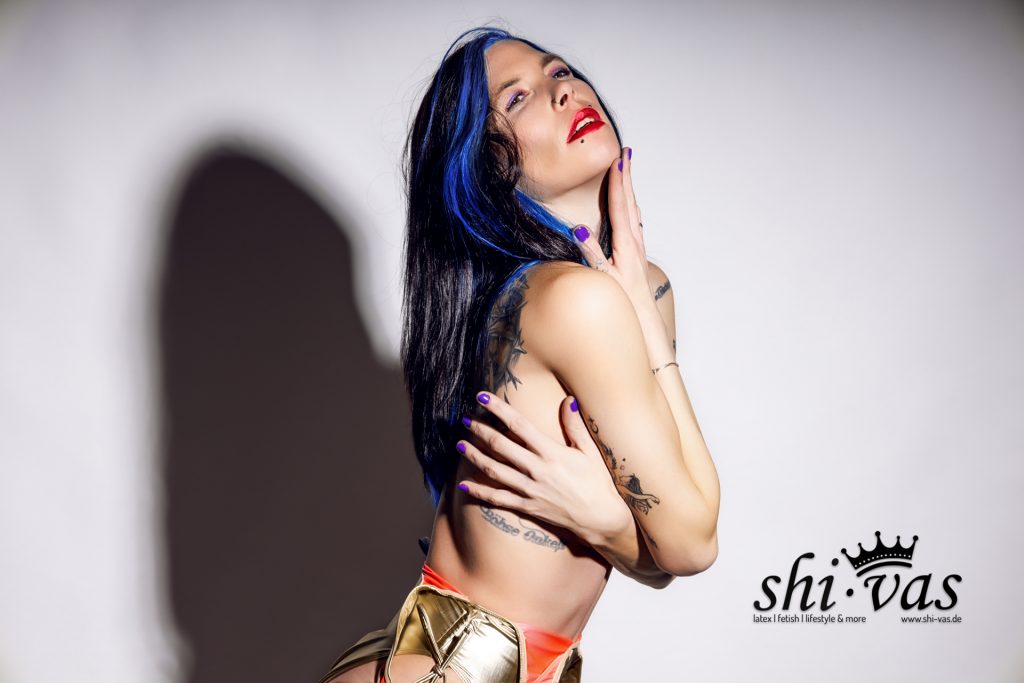 Coco in einer Seitenprofil-Pose, die Arme vor der Brust verschränkt, den Kopf in den Nacken gelegt und die Augen geschlossen. Sie trägt den goldenen Realise Badeanzug tief sitzend an der Hüfte.