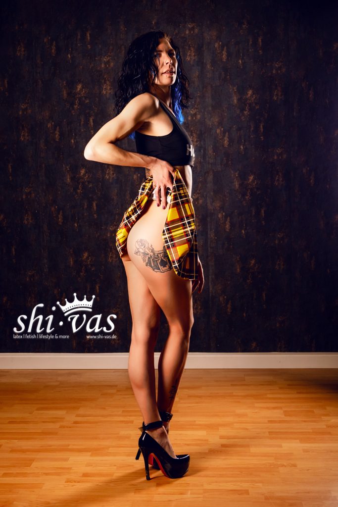 Coco in Seitenansicht hebt den Rock leicht an und zeigt ein großes Tattoo auf dem Oberschenkel