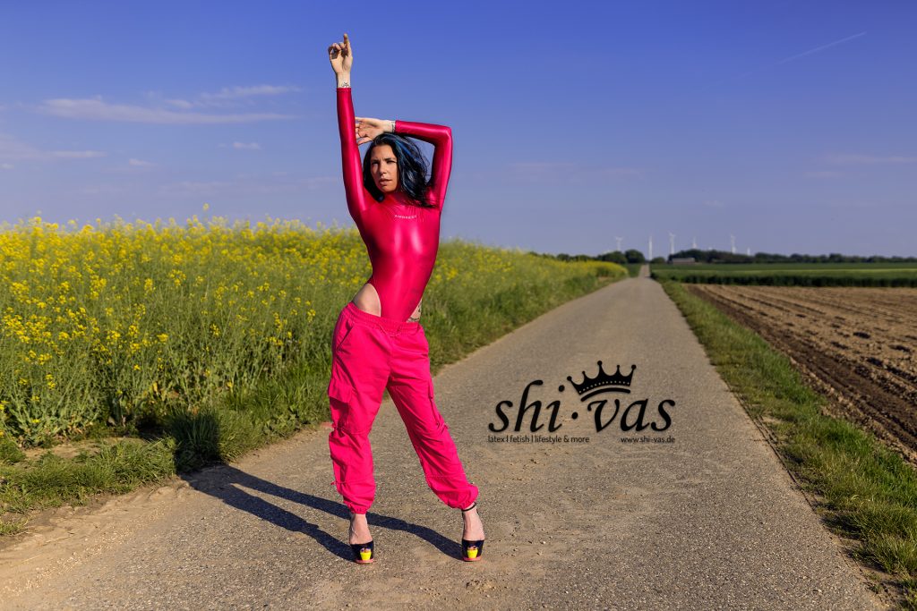 Coco streckt einen Arm hoch in die Luft, steht stabil und breitbeinig auf dem Weg, der Body spannt sich über ihren gesamten Körper.