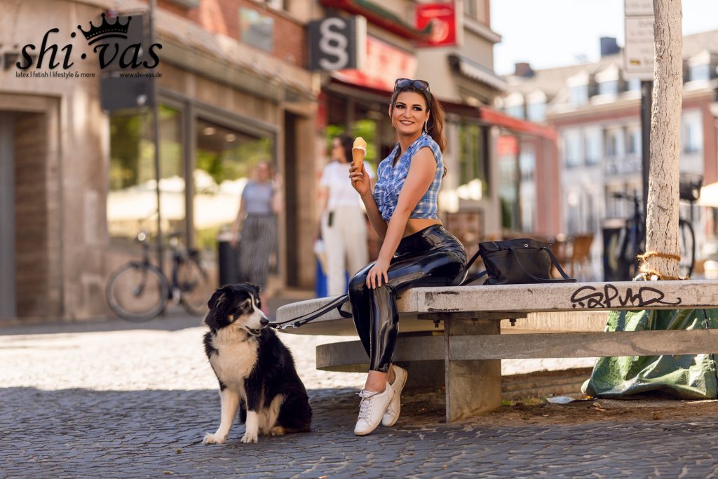 Lina sitzt auf der Steinbank, hält die Eiswaffel in der rechten Hand und blickt lächelnd direkt in die Kamera. Remo sitzt vor ihr und schaut nach links.
