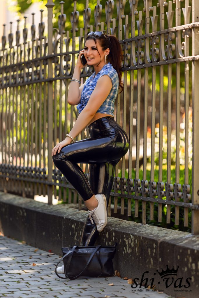 Lina sitzt auf einer Mauer am Zaun und telefoniert lachend mit einem Smartphone.
