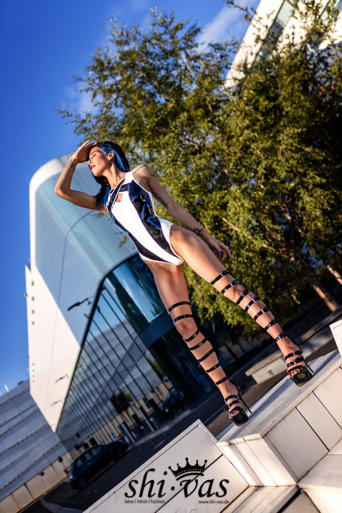 Model Coco steht in extrem hochgeschnittenem Latex-Bodysuit erhöht im Sonnenlicht und schirmt ihre Augen mit der Hand ab