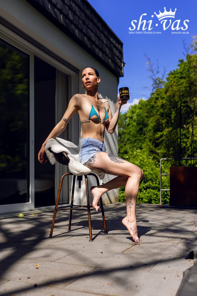 Coco posiert im blauen Bikini-Top und engen Jeans-Shorts auf einem Barhocker im Freien.