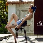 Coco räkelt sich im blauen Bikini-Top und Shorts mit angehobenem Bein auf einem Barhocker.