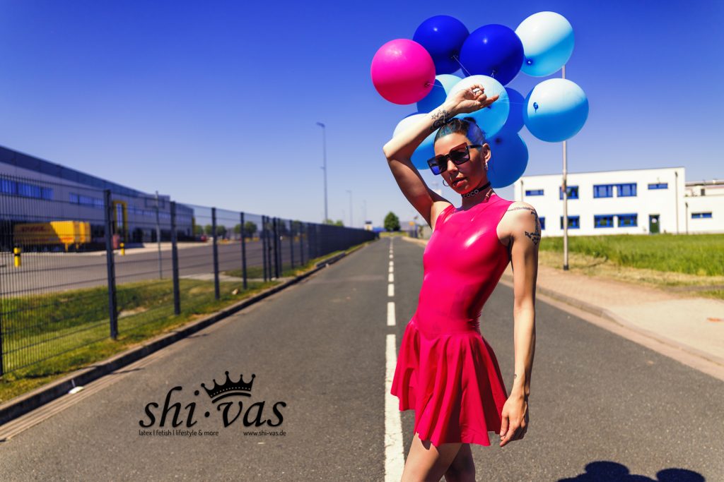 Coco im pinken Latexkleid mit Luftballons im gleißenden Sonnenlicht auf einer Straße