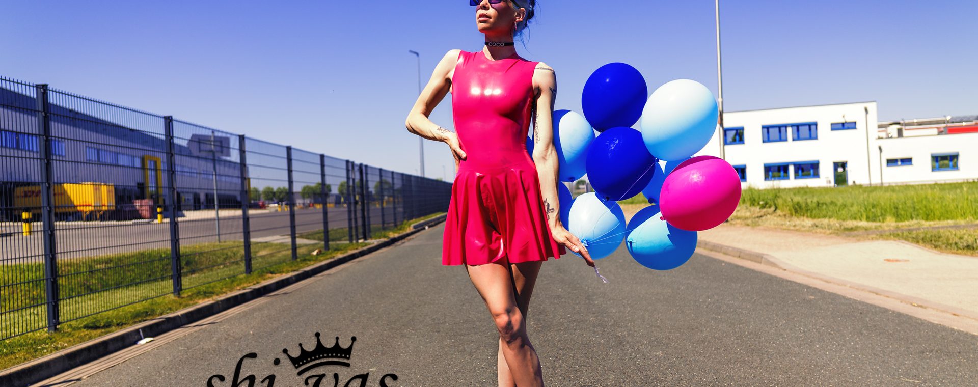 Coco im pinken Latexkleid mit Luftballons und Sonnenbrille auf einer Straße
