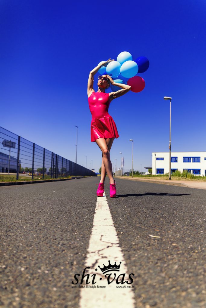 Coco im pinken Latexkleid mit Luftballons und pinken High Heels auf der Straße