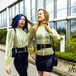 Coco und Lilly im identischen Latex-Look lächeln sich im Freien an.