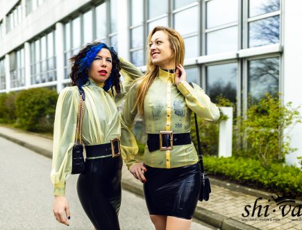 Coco und Lilly im identischen Latex-Look lächeln sich im Freien an.